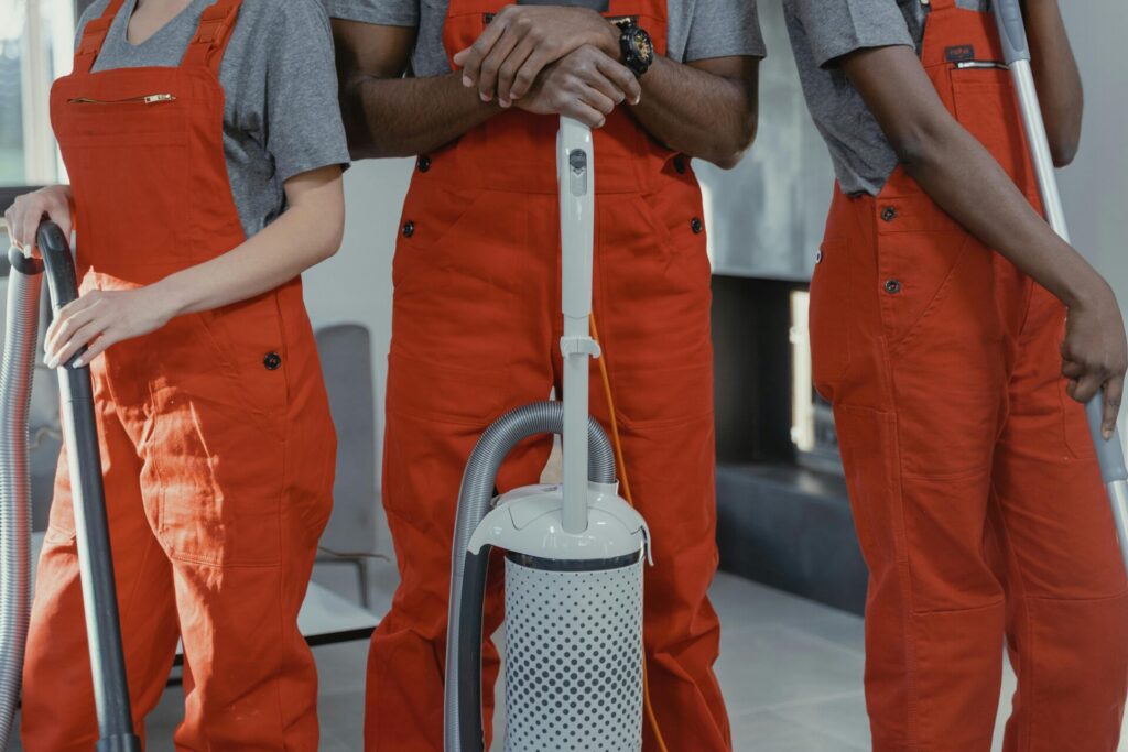 pexels-photo-6195129-6195129 Three workers in red coveralls with cleaning tools in a room.