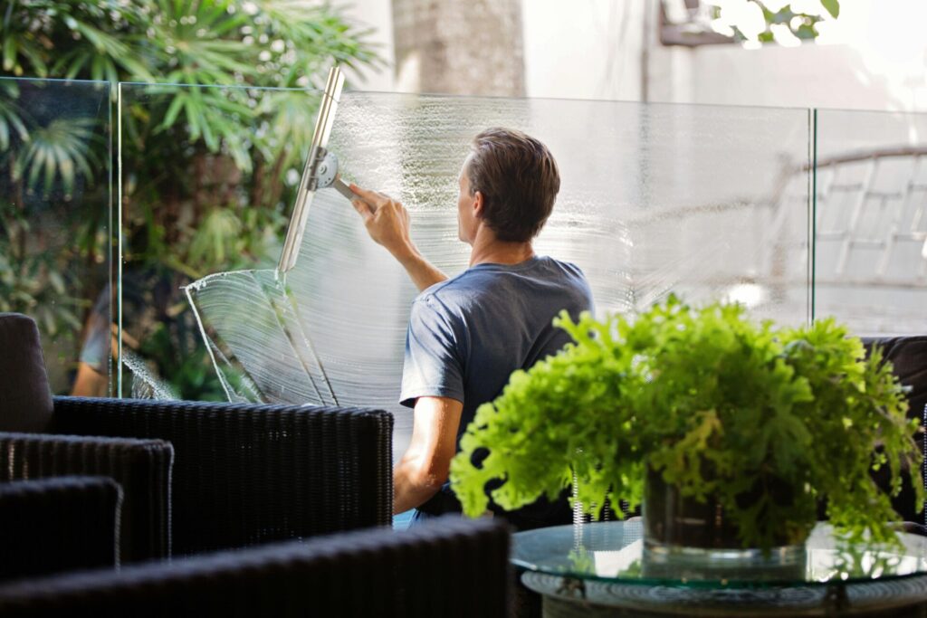 pexels-photo-713297-713297 A man cleaning a glass barrier outdoors with a squeegee, surrounded by greenery.